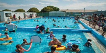 The school pool at Rawhiti school shows children playing in the water while adults watch from the sideline