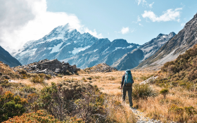 A man walks along a trail, a mountain looms in the background