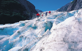 Three people walk up the side of a glacier in New Zealand