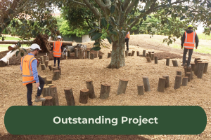 Four workers with high vis vests on and hard hats walk around logs that have been pushed into the ground